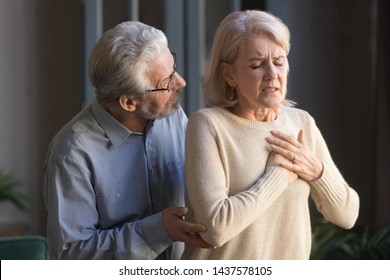 Worried Elder Senior Husband Helping Supporting Mature Middle Aged Wife Touching Chest Having Heart Attack Feeling Sudden Pain Heartburn Heartache Hurt At Home, Old Couple Health Problems Concept