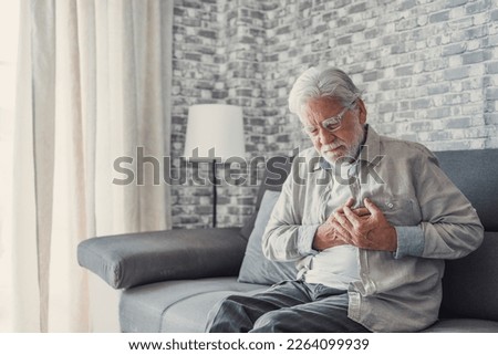 Worried elder senior man feeling bad, upset old middle aged grandfather touching chest feel sudden pain heartburn having heart attack sit on sofa at home