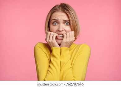 Worried female looks nervously, bites finger nails, watches moving strilling film, anticipates what end will be. Nervous excited young woman worries before job interview, wants to show her best