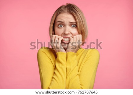Worried female looks nervously, bites finger nails, watches moving strilling film, anticipates what end will be. Nervous excited young woman worries before job interview, wants to show her best