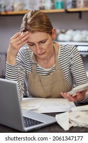 Worried Female Owner Of Coffee Shop In Financial Difficulty Looking Through Bills Using Laptop And Calculator