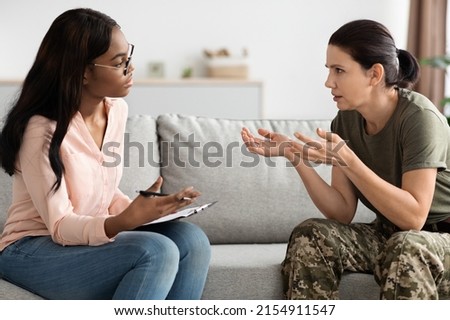 Worried female soldier talking to black psychologist during therapy session at office, african american psychotherapist lady listening emotional woman in military uniform, closeup shot