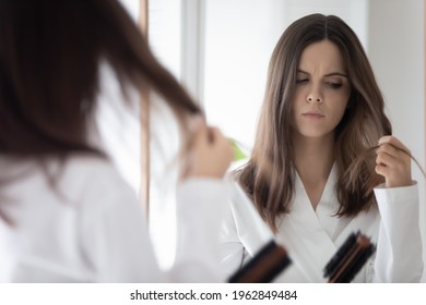 Worried girl concerned about hair loss, combing at mirror, holding hair brush and lock. Upset young woman counting fell out hairs. Haircare, health problem concept. Mirror reflection head shot - Powered by Shutterstock