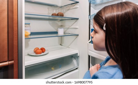 Beunruhigtes Mädchen, das den fast leeren Kühlschrank aufgrund einer Krise betrachtet