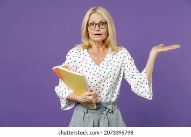 Worried Gray-haired Blonde Teacher Woman Lady 40s 50s Years Old In White Dotted Blouse Eyeglasses Standing Hold Notepads Spreading Hands Isolated On Bright Violet Color Background Studio Portrait