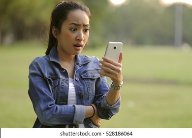 Worried Hipster Teenager Girl Looking At Her Smart Phone In A Park With An Unfocused Background