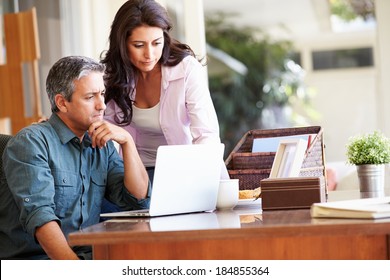 Worried Hispanic Couple Using Laptop On Desk At Home