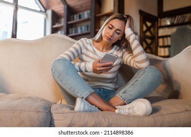 Worried Lady Looking At Smartphone Screen, Sitting On Couch At Home, Concerned Middle Aged Woman Waiting For Important Call, Reading Unpleasant Sms, Spending Time Holding Phone In Living Room