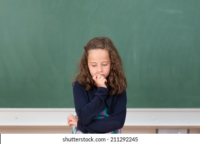 Worried Little Girl In School Sitting At Her Desk In Front Of The Blank Blackboard Staring Morosely Down At Her Class Notes