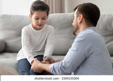 Worried loving young single father holding hand talking comforting upset little kid son sharing helping with problem, caring dad foster parent give support apologizing supporting listening child boy