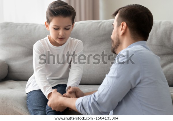 Worried loving young single father holding hand\
talking comforting upset little kid son sharing helping with\
problem, caring dad foster parent give support apologizing\
supporting listening child\
boy