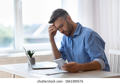 Worried Male Freelancer Looking At Smartphone Screen While Working At Home Office, Received Bad News, Got Scam Message, Thoughtful Man Touching Forehead With Concerned Face Expression, Copy Space