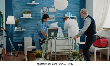 Worried Man Asking Medical Team To Help Sick Old Wife In Nursing Home. Doctor And Nurse Rushing To Give Assistance To Ill Retired Patient Hyperventilating, Laying On Hospital Bed