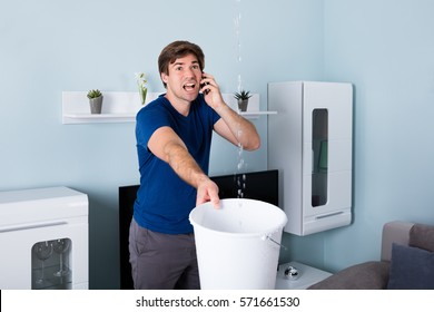 Worried Man Calling Plumber While Leakage Water Falling Into Bucket At Home - Powered by Shutterstock