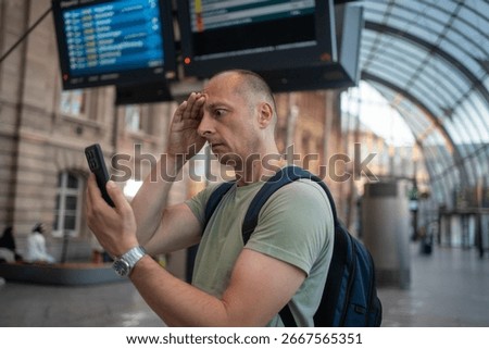 Worried man checking time while waiting for delayed public transport, frustrated by train or flight delay