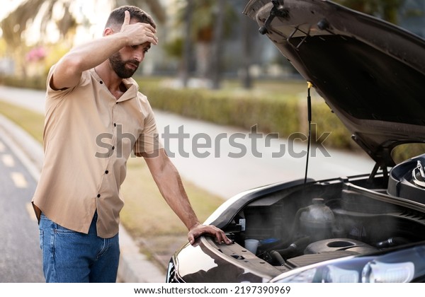 Worried man\
driver holding his head having engine problem standing near broken\
car on the road. Car breakdown\
concept