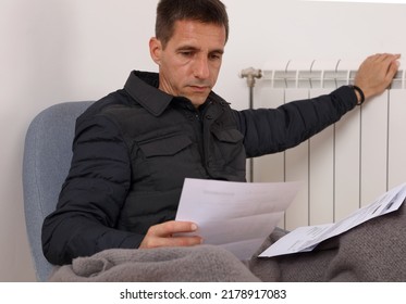 Worried man holding bills for electricity, gas and heating. Cold home, Global energy crisis concept - Shutterstock ID 2178917083