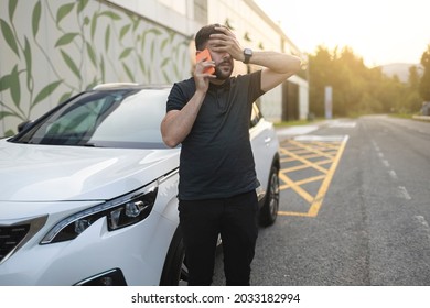 Worried Man Making Phone Call While Is While Is Covering His Eyes With Hand After Car Breakdown. Is Wearing Black Clothes. White Car Parked Near Road