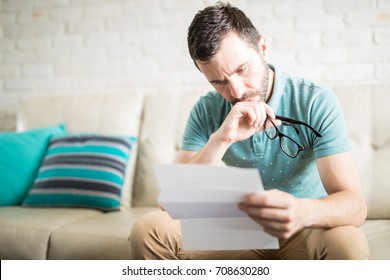 Worried Man Reading His Mail And Monthly Bills And Holding His Glasses In His Hands