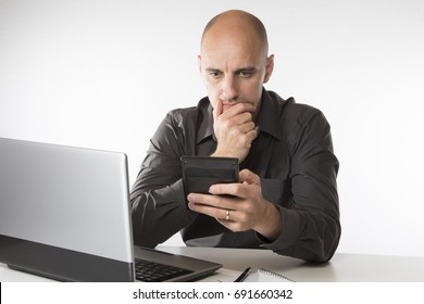 Worried man staring at a handheld calculator as he sits at his desk working on a laptop computer - Shutterstock ID 691660342