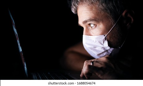 Worried Man Wearing Face Mask Looks Through A News Site On His Laptop. Latest Coronavirus Outbreak Information Related Shot