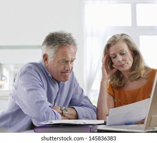 Worried Mature Couple With Bills Sitting At Dining Table In House