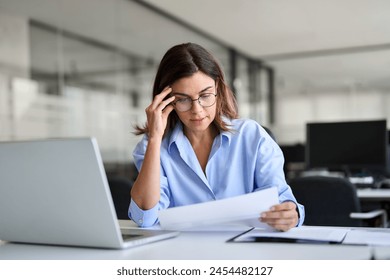 Worried mature professional business woman reading bad news in document at work. Tired upset busy 40s middle aged businesswoman feeling stress looking at paper bill having problem in office. - Powered by Shutterstock