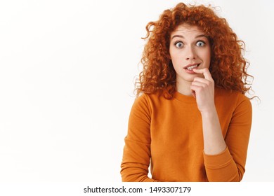 Worried Messy Cute Redhead Female Realise Making Tiny Mistake Feel Awkward And Embarrassed, Biting Finger From Concern, Stare Camera, Eager To Try New Chocolate Flavor, Standing White Background