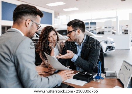Worried middle age man with his wife buying car in auto salon or showroom. He is hipped while woman asks him to still buy a car.