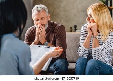 Worried Middle Aged Couple Sitting On Sofa With Financial Advisor At Home