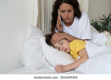 Worried mom calling to family doctor checking temperature of sick kid lying in bed. Small preschool boy suffer of fever from coronavirus or influenza sleep covered with blanket. Child cure and health