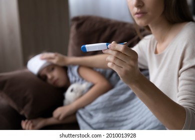 Worried mom treating sick kid suffering from flu and fever, holding thermometer, checking high body temperature, applying cold compress on forehead. Childcare, kids healthcare concept