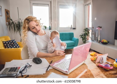 Worried Mother Holding Baby And Talking On Smart Phone At Home Office