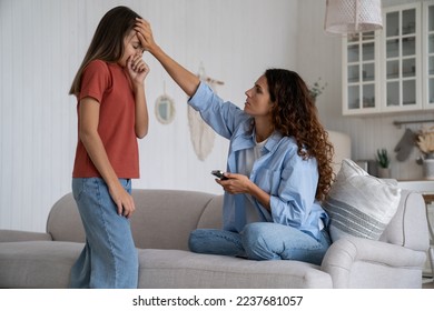 Worried mother holding mobile phone touching forehead of unhealthy coughing daughter, mom parent calling to doctor pediatrician, teen girl get sick, feeling unwell. Colds in children, caring for kids - Powered by Shutterstock