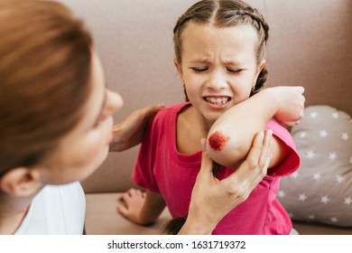 Worried Mother Looking At Bloody Elbow Of Crying Daughter