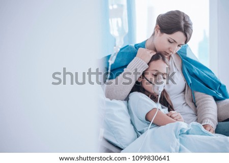 Worried mother taking care of her daughter wearing an oxygen mask in the hospital