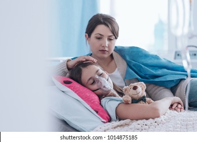 Worried mother taking care of a kid with cystic fibrosis lying in hospital bed with plush toy