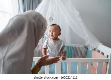 Worried Mother Try To Comfort Her Cry Child At The Crib. Separation Anxiety