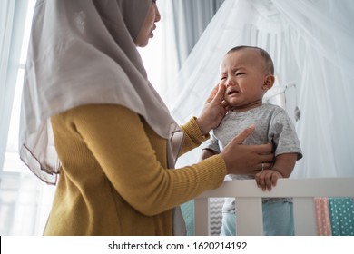 Worried Mother Try To Comfort Her Cry Child At The Crib. Separation Anxiety