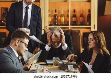 Worried Old Chairman Leaded Over Conference Desk Grabbed Gray Head With Hands, Serious Woman Holding Pen Thoughtfully Pointing To Diagram Not Looking At Camera