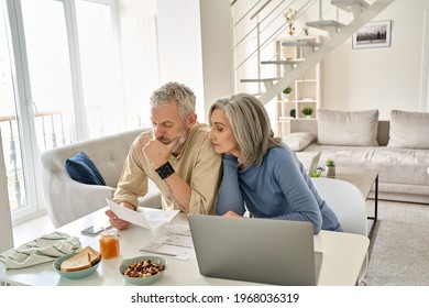 Worried Old Senior Couple Checking Bank Documents At Home. Serious Mature Retired Family Reading Paper Bills, Calculating Taxes, Planning Retirement Finances, Household Expenses, Having Money Problems