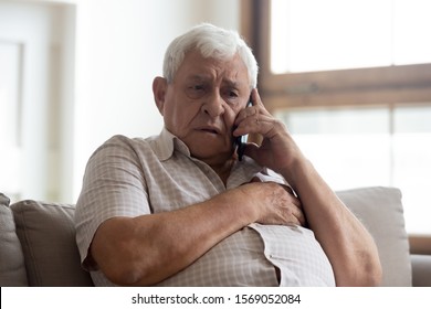 Worried Older Unhealthy Man Sitting On Couch, Making Emergency 911 Call, Having Painful Feelings In Chest, Heart Attack Disease Symptoms. Unhappy Frustrated Elderly Grandfather Listening To Bad News.