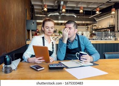 Worried owners in empty restaurant calculating finances - Coronavirus pandemic crisis - Bankrupt concept of Small entrepreneurs SME - Overwhelmed young woman and man with headache - Shutterstock ID 1675333483