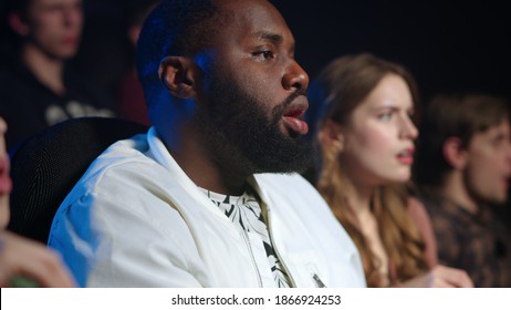 Worried People Watching Film In Movie Theater. Shocked African Man Looking To Girl Near In Cinema. Surprised Friends Eating Popcorn In Dark Hall.