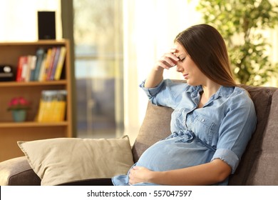 Worried pregnant woman sitting on a couch in the living room at home - Powered by Shutterstock