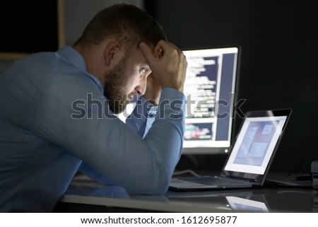 Worried Programmer Working Late At Night On Multiple Computer Screens