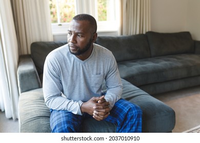 Worried, Sad African American Man Thinking, Sitting On Couch Looking Out Of Window In Living Room. Spending Time Alone At Home.