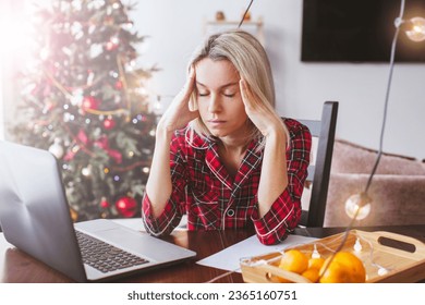 Worried sad middle aged woman working at the home office during Christmas holiday. Stressed upset female looking at screen of laptop by Christmas tree - Powered by Shutterstock