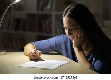 Worried sad woman signs contract at night sitting in the living room at home