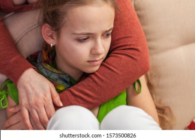 Worried and sad young girl sitting on sofa - woman embracing and comforting her. Teenage problems concept.